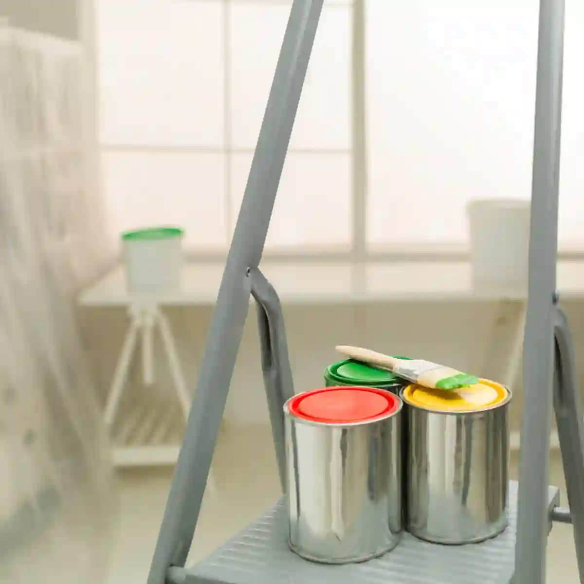 Step ladder with red, yellow, and green paint cans and a brush. Setup for a residential painting project with vibrant colour options and prep materials.
