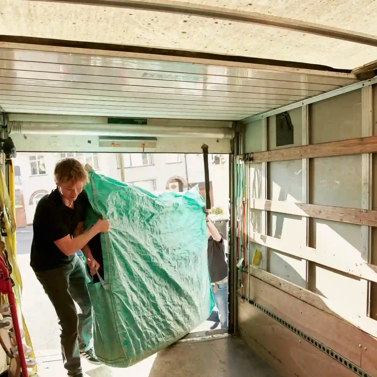 Rubbish removal team loading a large, covered item into a truck in a residential area. Professional clean-up and disposal service for bulky household waste in Australia.