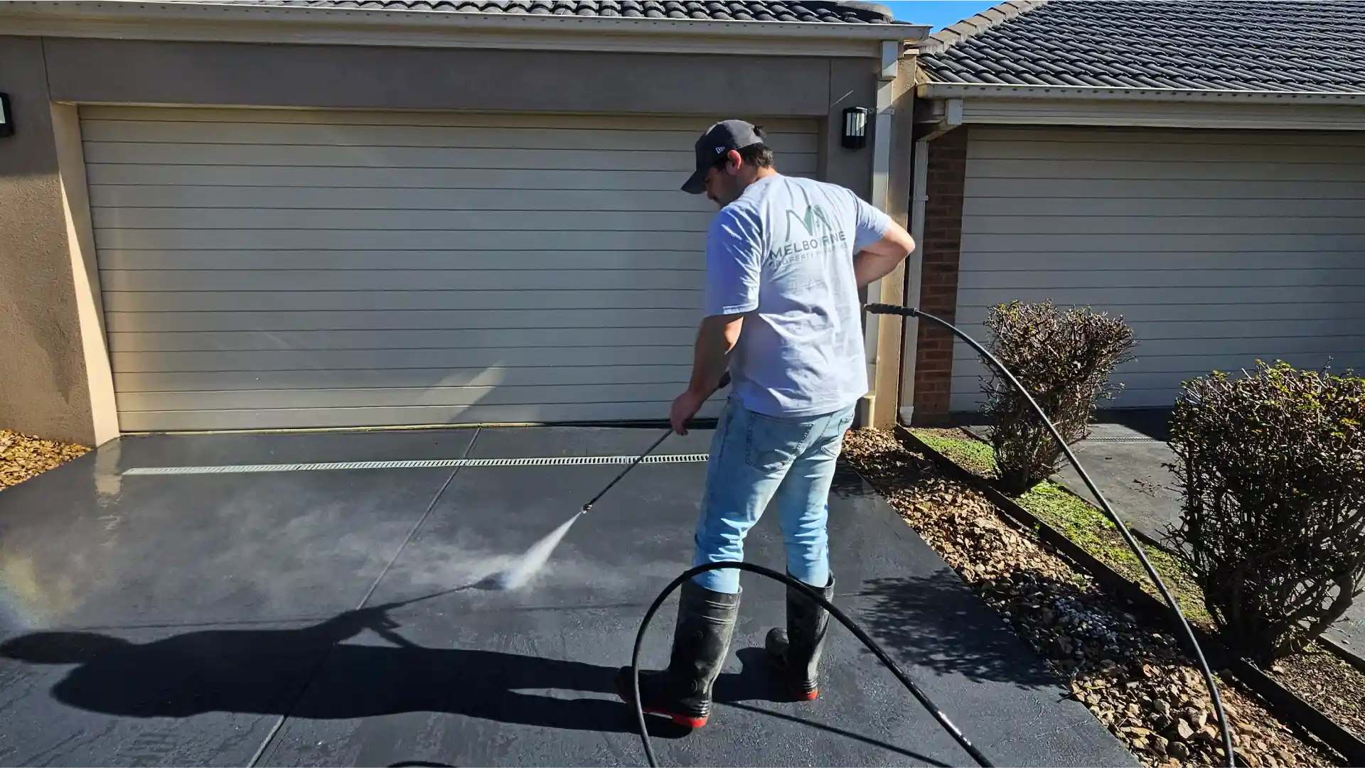 Melbourne Property Preparers team member pressure washing dark concrete driveway in Melbourne to remove dirt and stains and enhance curb appeal during residential property maintenance