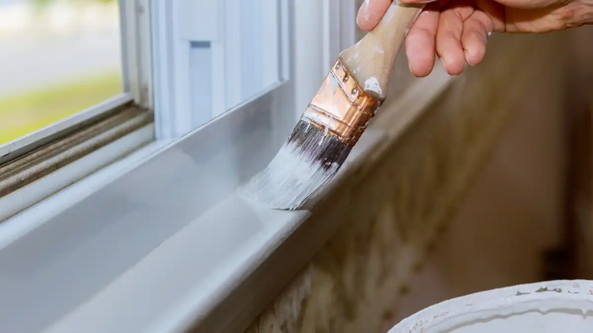 Close up of a man hand carefully painting the edge of an house window.